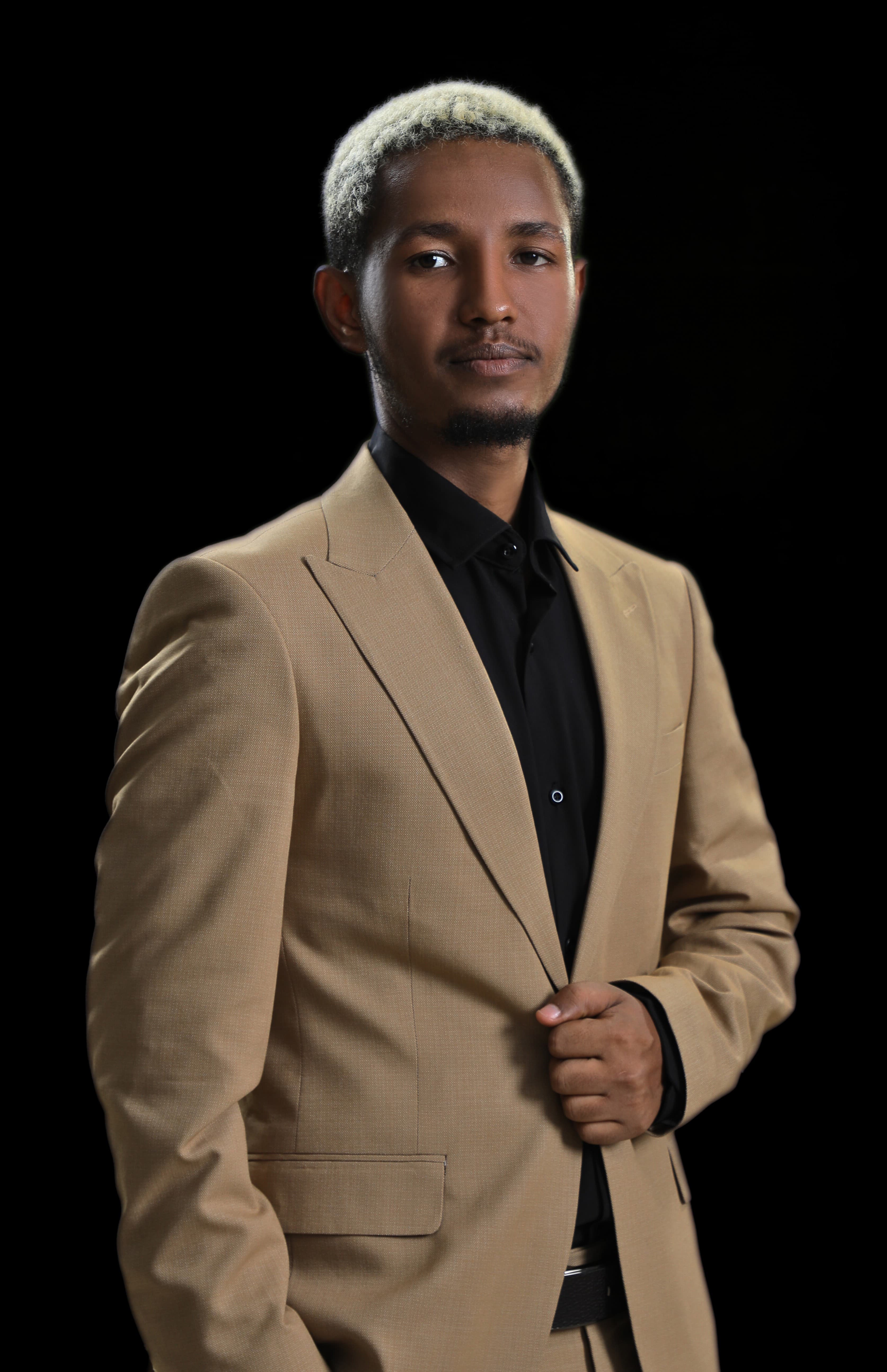 Smachew Gedefaw in a tan suit and black shirt, photographed against a black background.